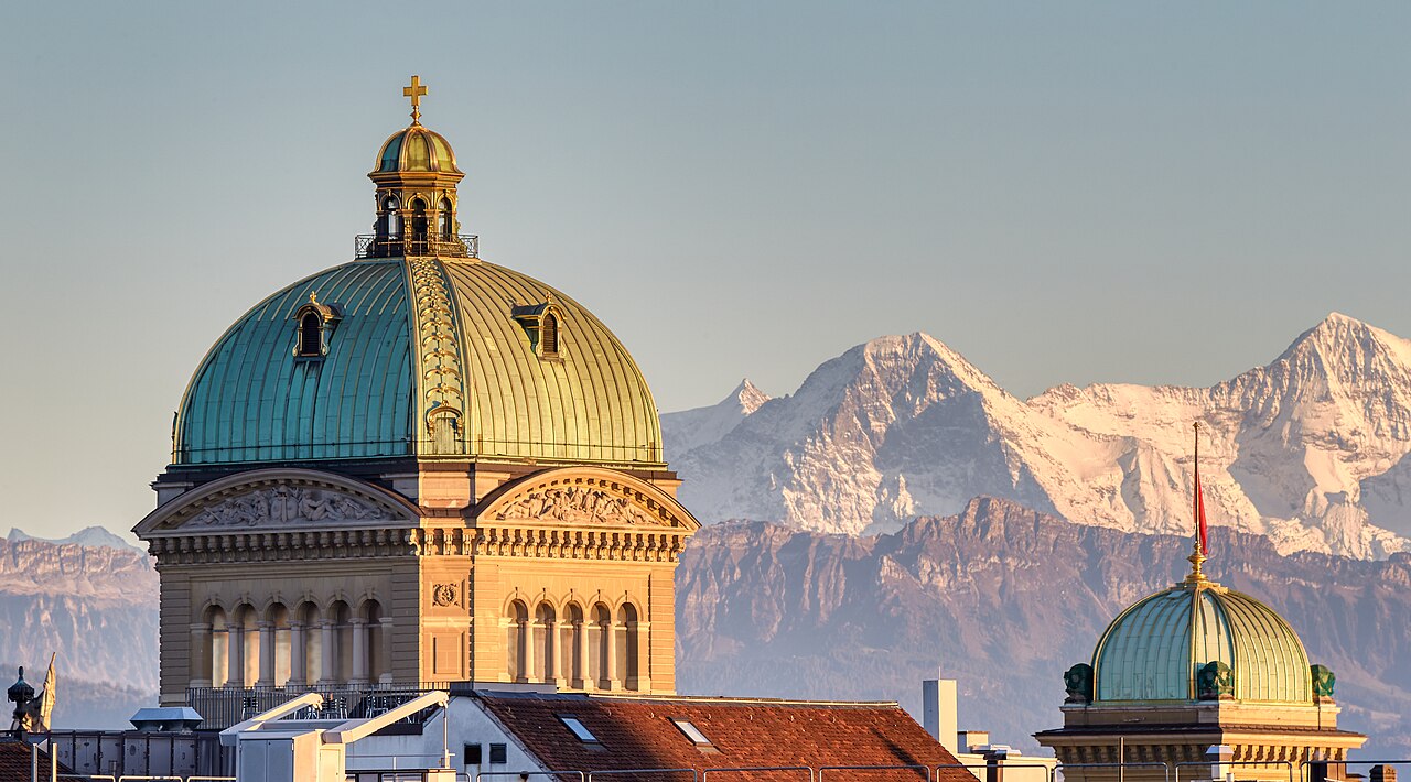 The Federal Palace in Bern in evening light, with the Eiger and Mönch behind